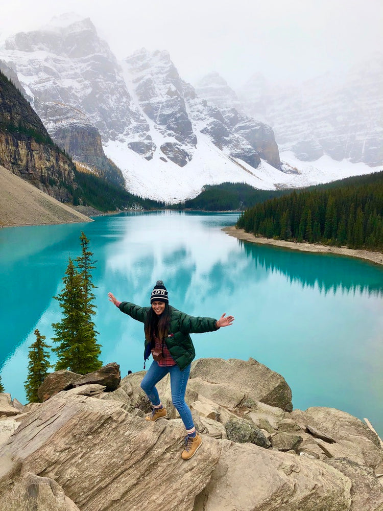 Jessica S, founder of WANDRVEL, arms outstretched above a turquoise mountain lake